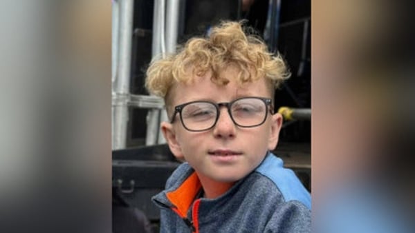 A young boy with blonde curly hair and glasses poses for a pictue