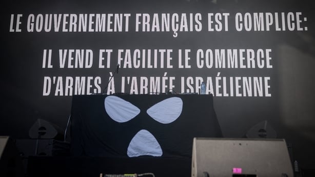 This photograph shows a slogan that reads "The French Government is complicit: it sells and facilitates the arms trade to the Israeli army" screened on stage ahead of Kneecap's set at the Rock en Seine music festival, in Saint-Cloud, near Paris, on August 24, 2025
