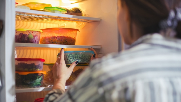 An image of an unrecognizable person reaching for certain containers in the fridge. They're all filled with chopped veggies or fruits.