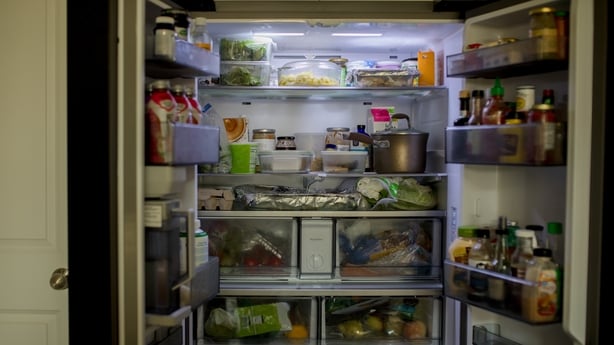 A well-stocked side-by-side fridge with its doors wide open, displaying an array of food items, from condiments to snacks, perfect for promoting home organization