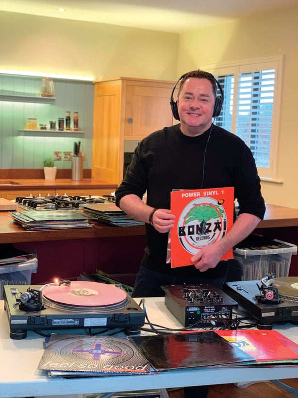 Neven Maguire standing in his kitchen in front of a turntable with vinyl records