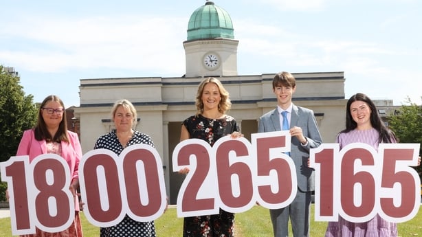 Students flank Min Helen McEntee at Government Buildings holding foam numbers 1800265165.
