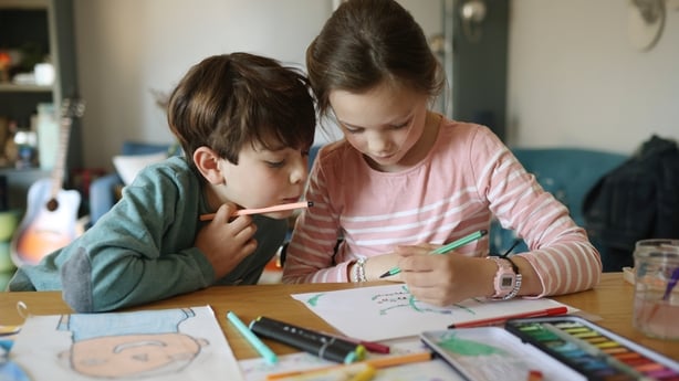 A girl and her little brother drawing on the living room table