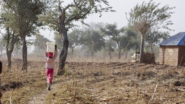 a girl walks through rural area in Nigeria carrying a bucket on her head