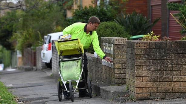 A postman in a high vis jacket delivers mail into boxes outside a building 
