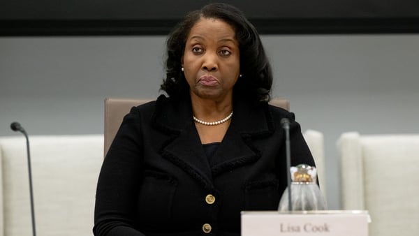 A woman in a black suit sits at a board table