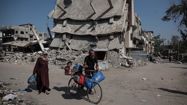 A man with a bicycle is seen walking in front of a destroyed building in Gaza with a woman and child behind him