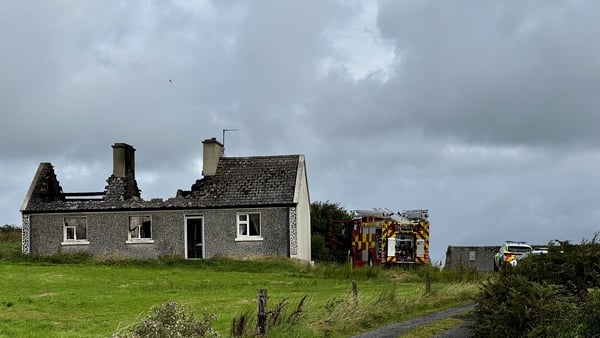 A house damaged by fire with a fire engine in the background
