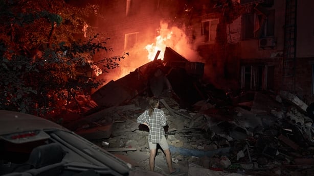 A person looks on as flames rise from a building hit by a Russian missile in Kyiv