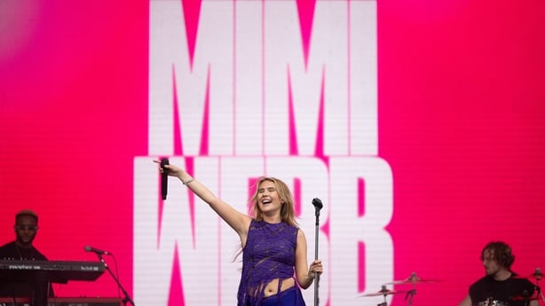 Mimi Webb performing on stage with her hand in the air