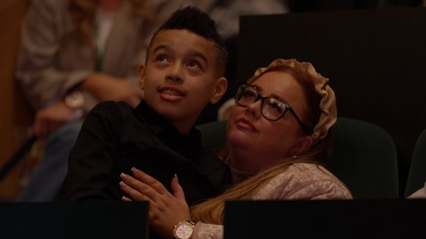 A toung boy and his mother look up in an embrace