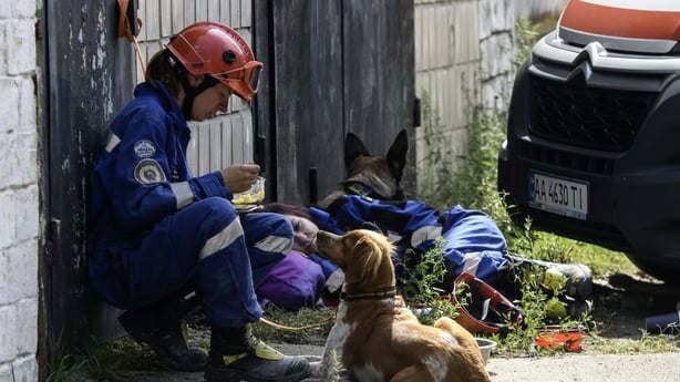 A rescue worker dressed in blue wearing a red helmet sits next to a dog