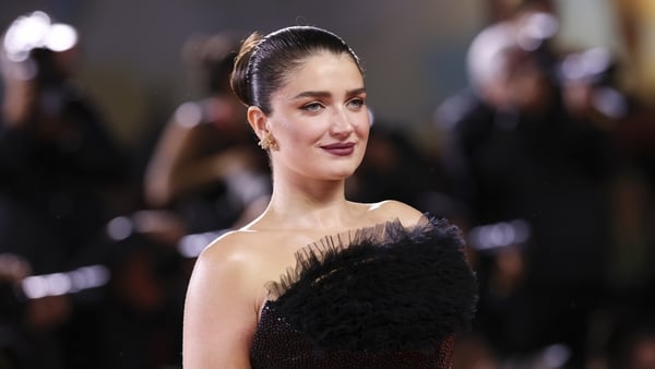 Eve Hewson wearing a black ruffled gown and smiling for photographers