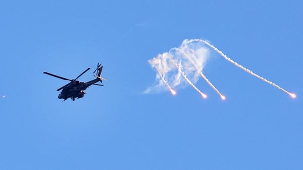 A black helicopter fires flares with a clear sky in the background