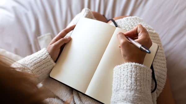 High angle view of a woman wearing a robe sitting on bed writing on journal in cozy bedroom
