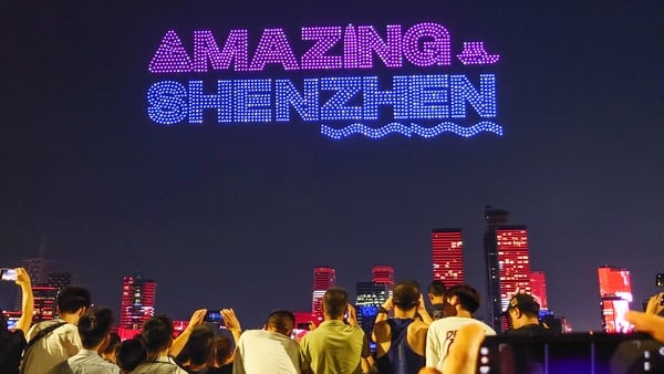 A drone light show spelling out Amazing Shenzhen in the sky over a group of people's heads