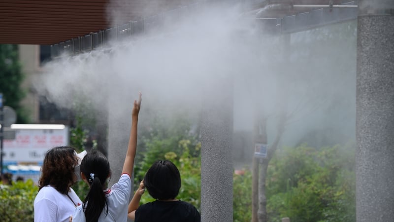 People stand under a cooling mist in Ginza district during high temperatures in Tokyo