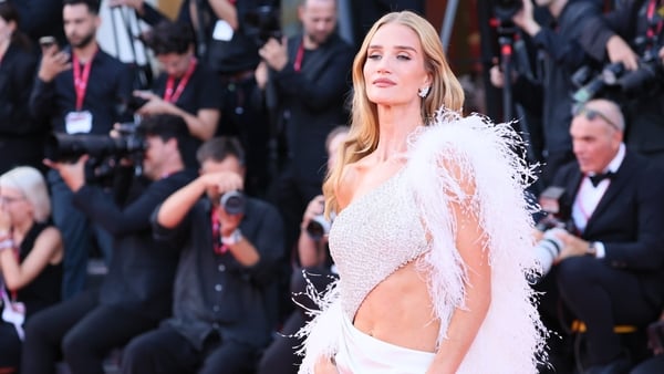 Rosie Huntington-Whiteley wears a white gown with cut-out detailing on the waist and a feathered boa