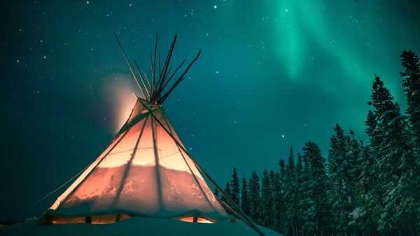 A tent in a forest with the Northern Lights overhead