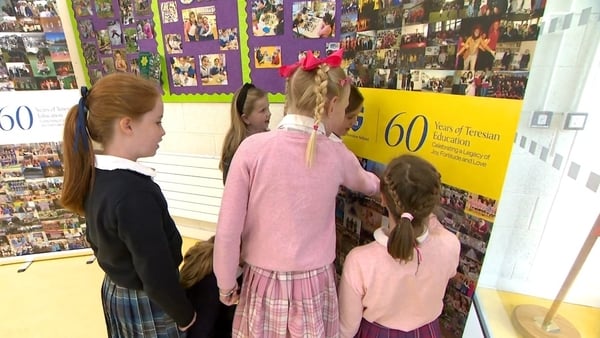 A group of young girls at school point to a poster on the wall.