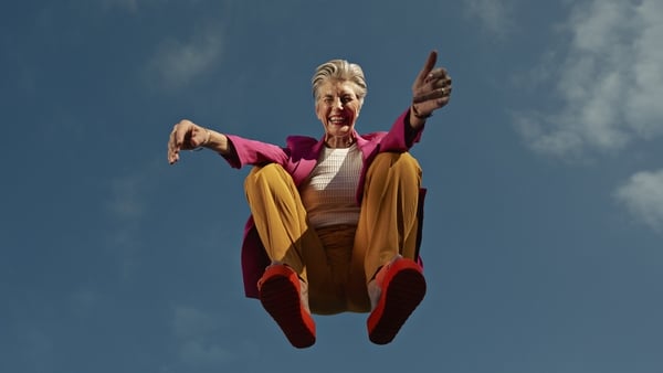 Directly below portrait of happy senior woman crouching mid-air against blue sky