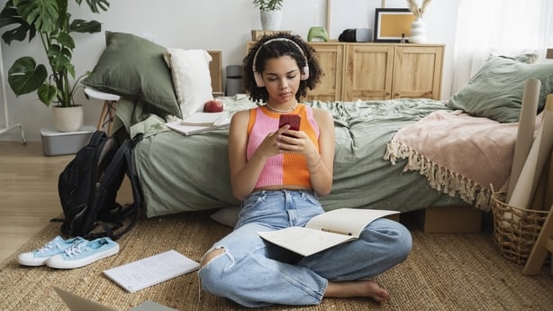 Teenage girl wearing wireless headphones using mobile phone on rug at home