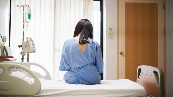 Young woman sitting in hospital bed with back to the camera