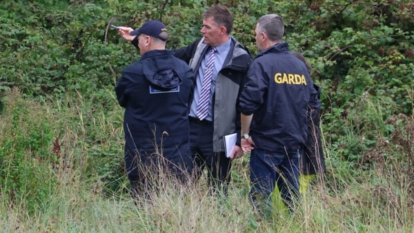 Three men wearing clothing with 'garda' written seen talking in a field