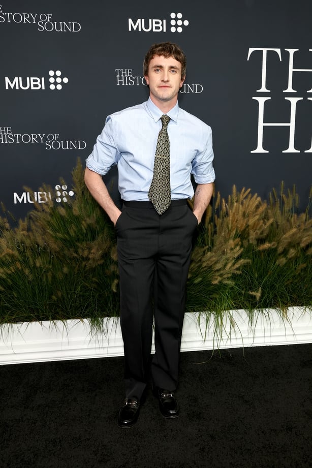 Paul Mescal poses for photos wearing a blue shirt, patterned tie and black trousers