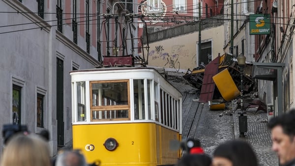 A yellow and white funicular tram car is seen in the foreground with wreckage of one which crashed in the background