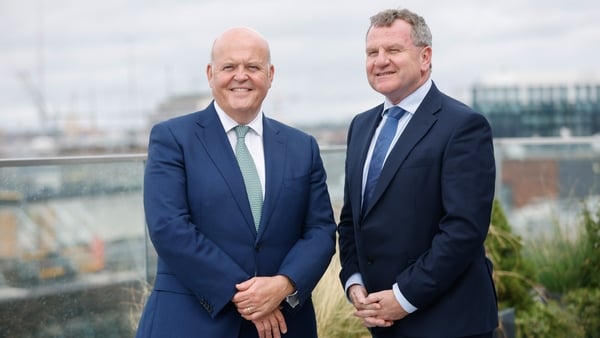 Two men in suits pose for a photo on a rooftop garden