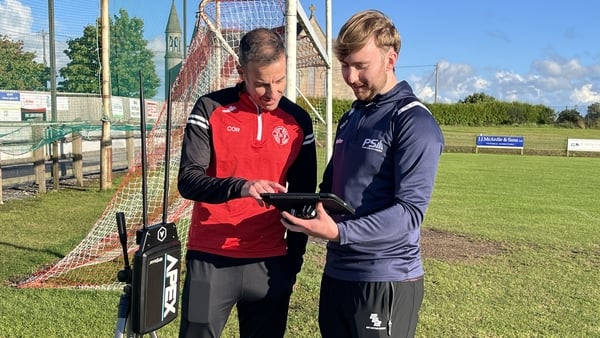 Two men look at a screen on a GAA pitch