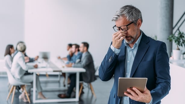 Shot of a overworked businessman standing in front of his team and using digital tablet. Portrait of stressed businessman standing with his colleagues working in background.