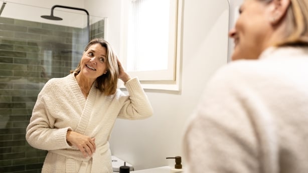 Smiling senior woman wearing bathrobe, looking at herself in the mirror and fixing her hair in the bathroom