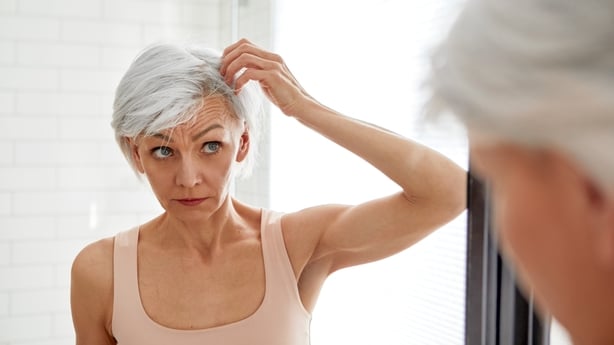 Senior beautiful woman standing in front of mirror looking in her hair