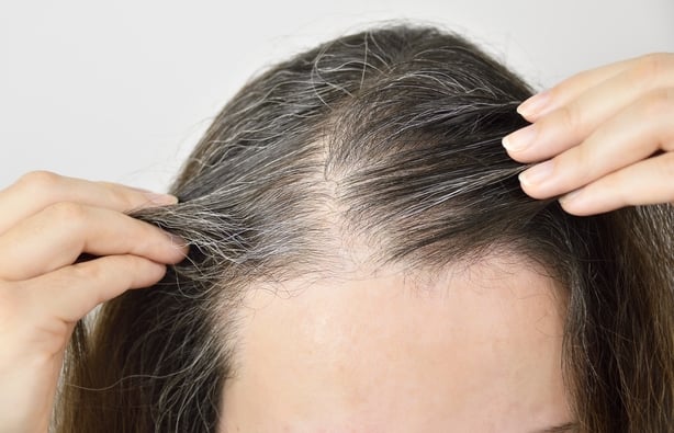 woman is checking white hair while looking at the mirror