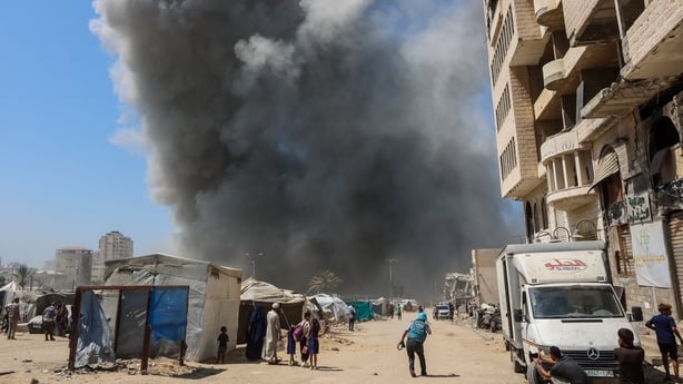 People watch from the street as smoke rises following an Israeli strike on the Mushtaha Tower in Gaza City