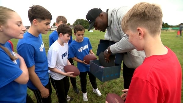 A group of children on a football pitch are shown an american football in a box.