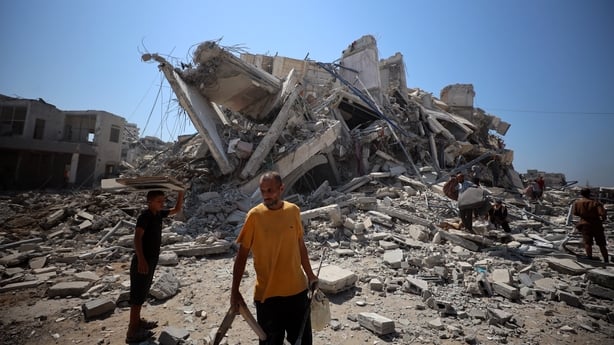 People walk among the rubble of the damaged Mushtaha Tower after it is destroyed in an Israeli airstrike