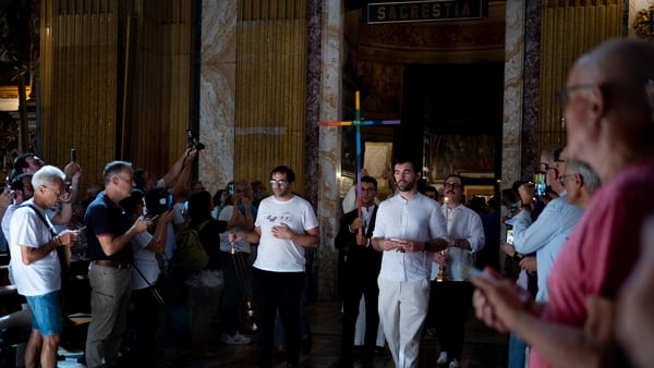 A man holding a cross arrives with other members of the LGBTQ+ community holding a crucifix in rainbow colours