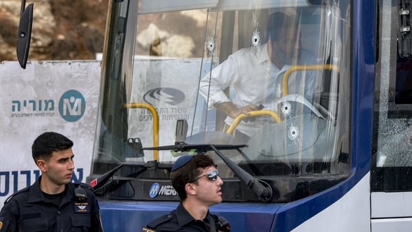 Two Israeli policemen walk past the windshield of a bus, riddled with bullet holes,