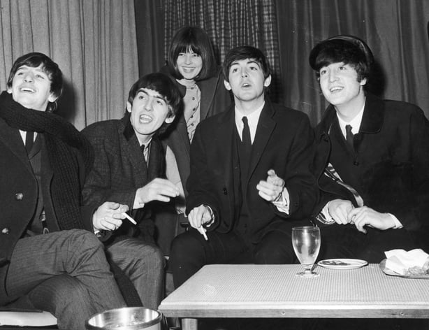 circa 1964: The British rock group The Beatles wear overcoats and smoke cigarettes while talking to reporters, including Maureen Cleave of the Evening Standard, who stands behind them. L-R: Ringo Starr, George Harrison (1943 - 2001), Paul McCartney and John Lennon (1940 - 1980). (Photo by Daily Expr