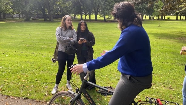 Teenage girl riding a bicycle in a park next to friends - RTE