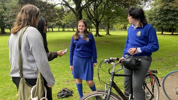 Teenage girls chat next to a bicycle in a park - RTE