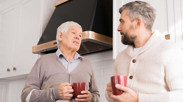 two men talk in a kitchen, holding mugs