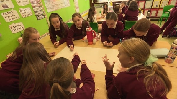 A group of girls sitting around a table at school discussing and writing down ideas on a large poster.