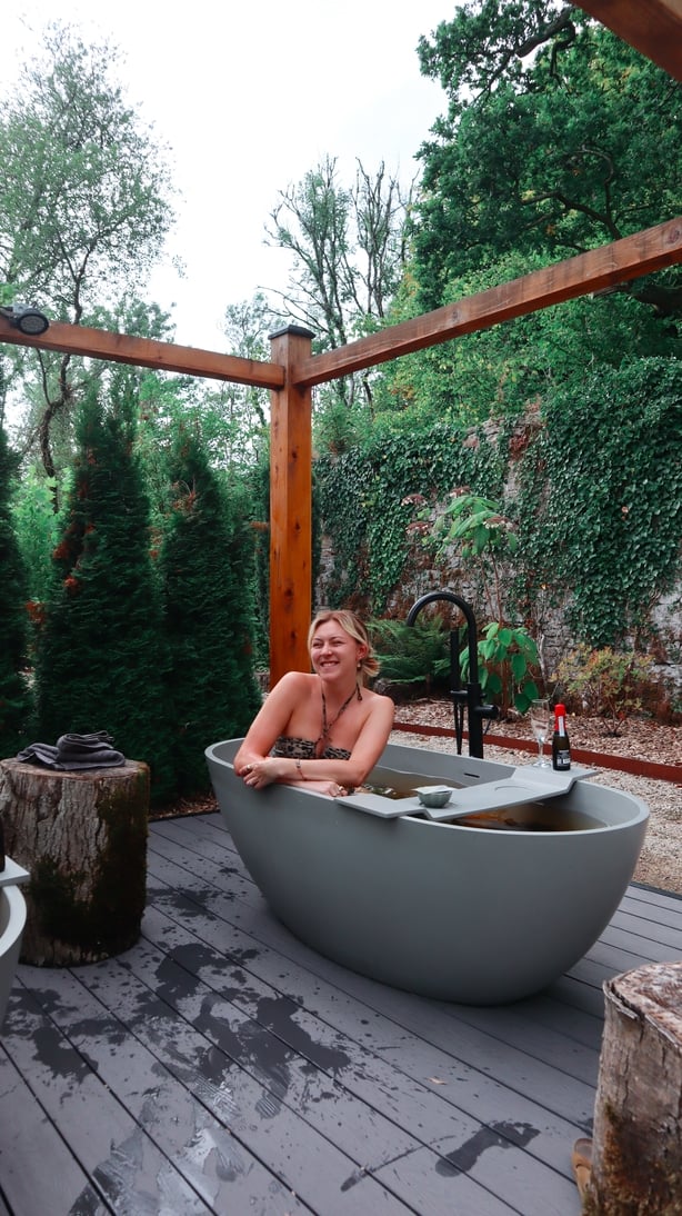 A woman sitting in an outdoor bath, smiling at the camera