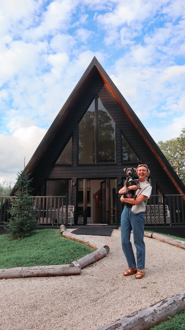 An A-frame building and a woman standing in front of it with her dog