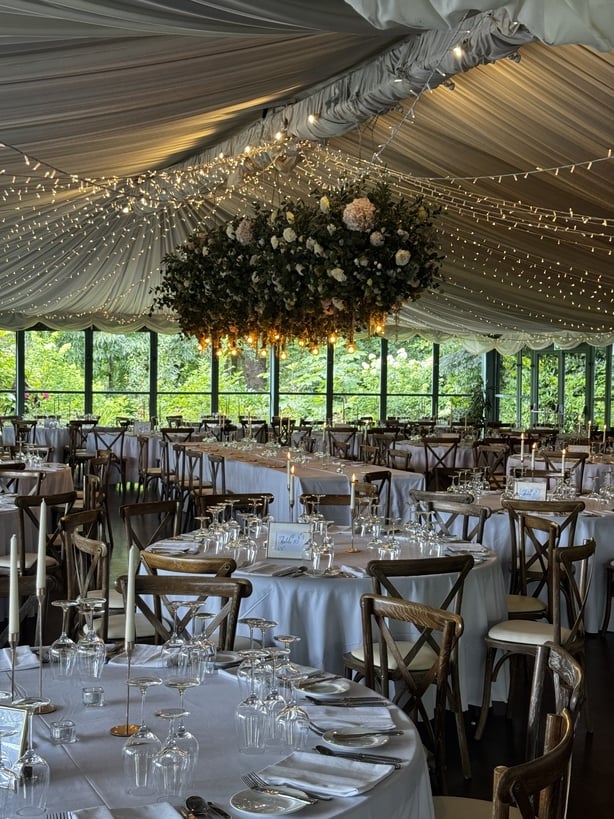 A reception room with bunting, fairy lights and flowers overhead