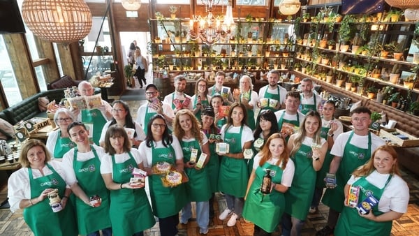 A group of people standing together holding Irish food products in green aprons by Aldi